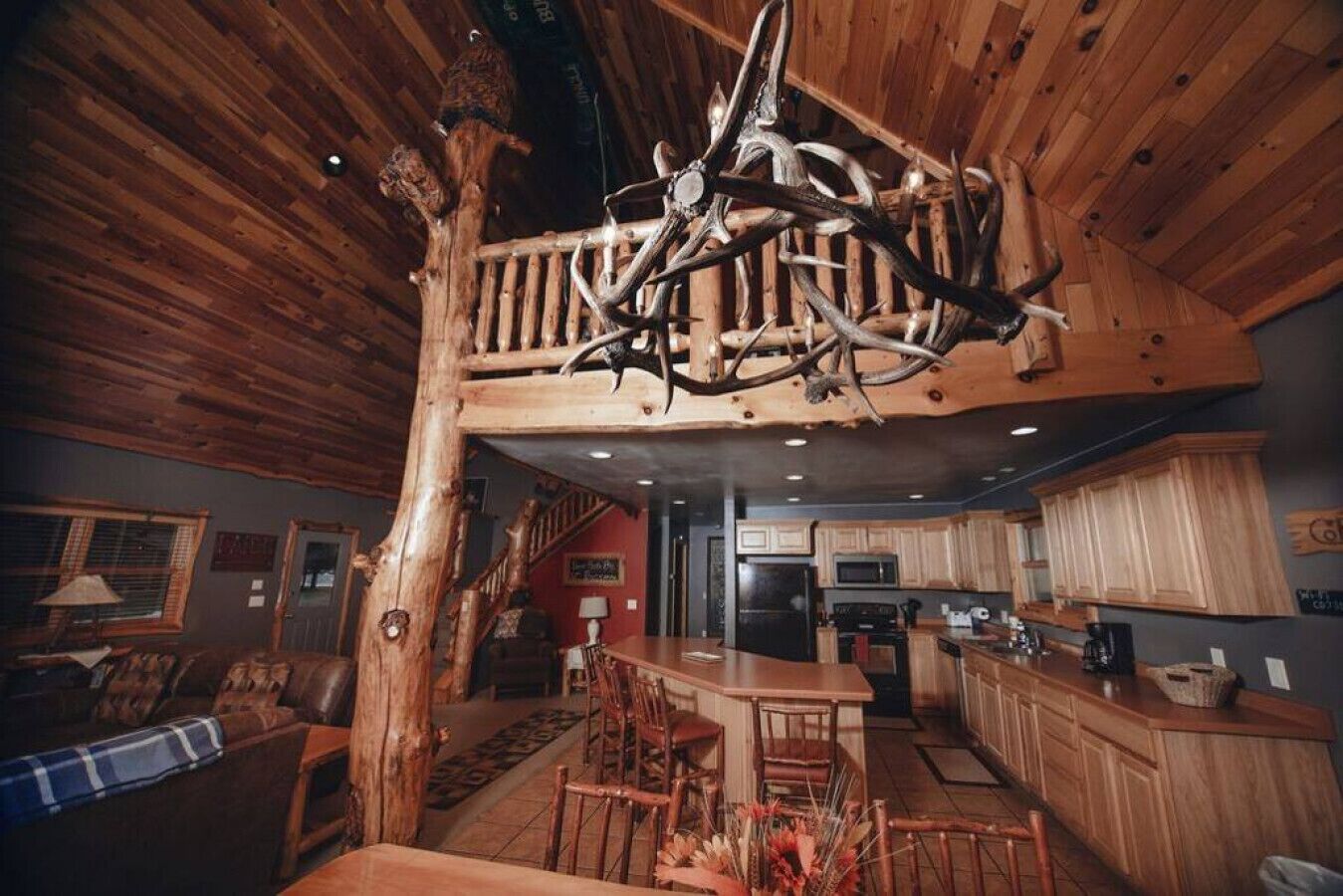 A rustic interior with a high ceiling, wooden beams, a dining area, kitchen, and a staircase.