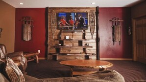 Ein Zimmer mit einer Holzwandverkleidung, auf der ein Fernseher steht, einem runden Holztisch, Ledersofas und einer roten Akzentwand.