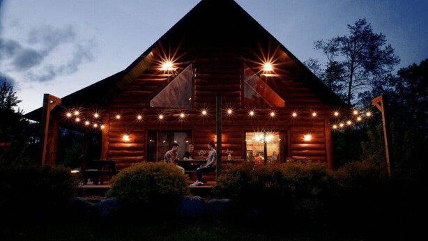 Eine Blockhütte mit Veranda, Sitzgelegenheiten im Freien und Lichterketten.