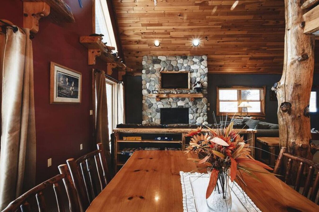 A wooden dining table with chairs, a stone fireplace, and a large window.