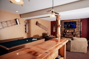 A pool table with a wooden bar in a room with a red wall, a television, and a wooden shelf.