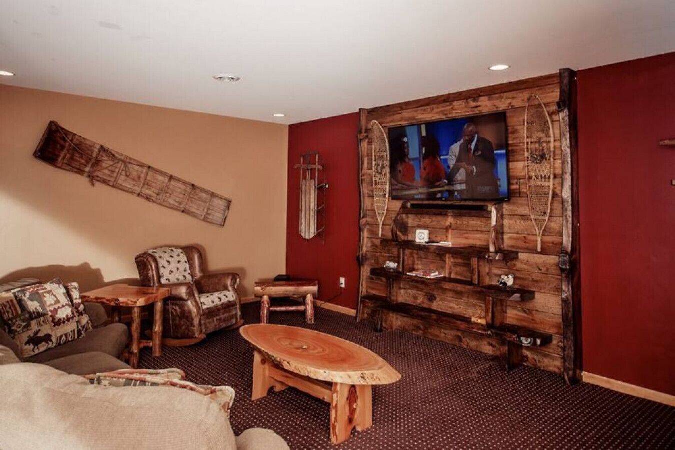 A living room with a large TV mounted on a wooden wall, a sofa, a coffee table, and a patterned rug.