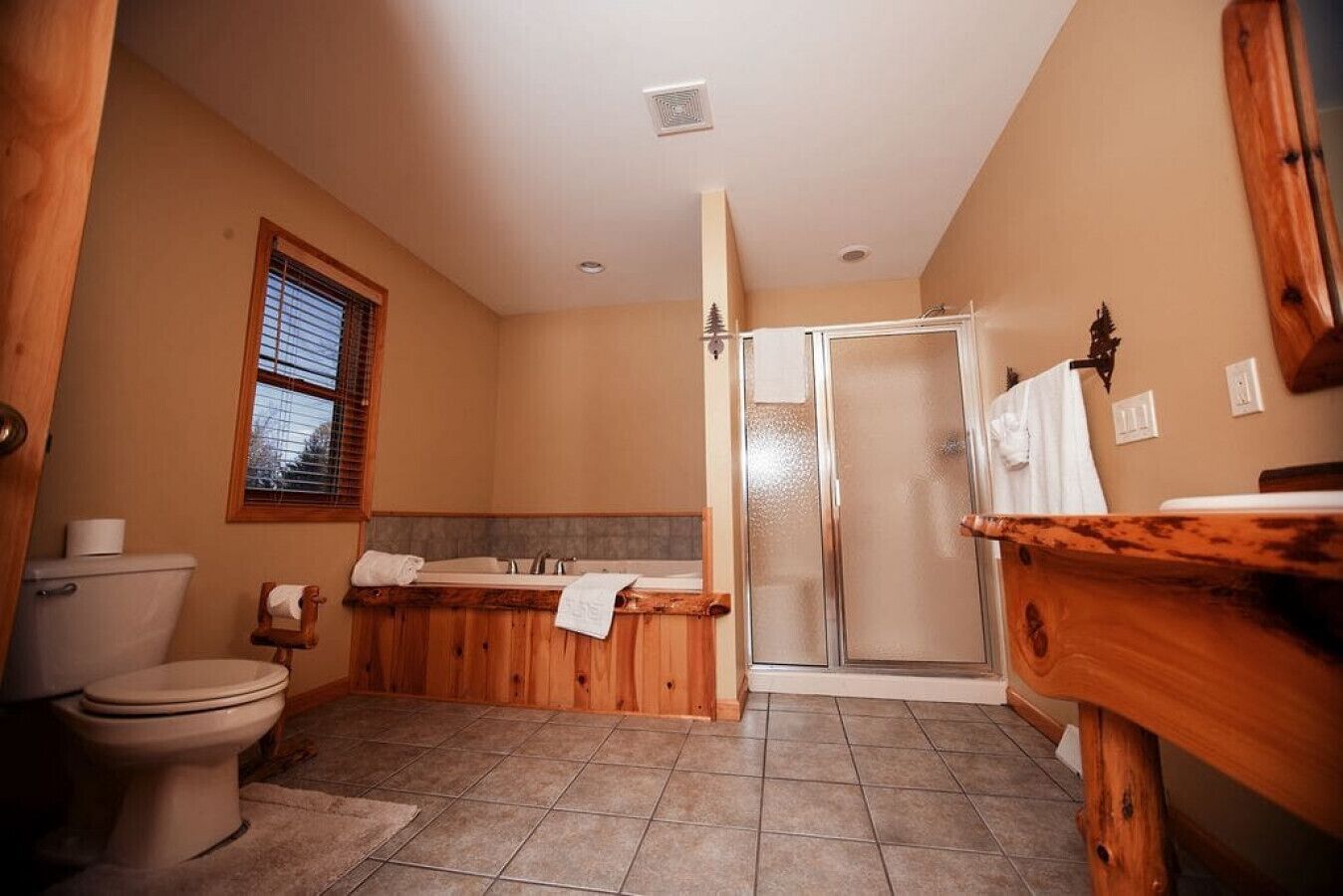 A bathroom with a toilet, a wooden bathtub, a shower, and a sink.