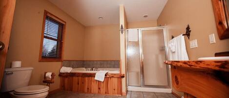 A bathroom with a toilet, a wooden bathtub, a shower, and a sink.