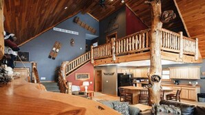 Ein großzügiger Wohnbereich mit einer Holztreppe, die in eine obere Etage führt, einer Küche mit Holzschränken und einer gemütlichen Sitzecke mit einer Ledersofa.