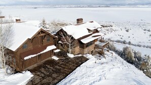 Une cabane en bois, dont le toit est recouvert de neige, située dans un paysage enneigé et offrant une vue dégagée sur les montagnes lointaines.