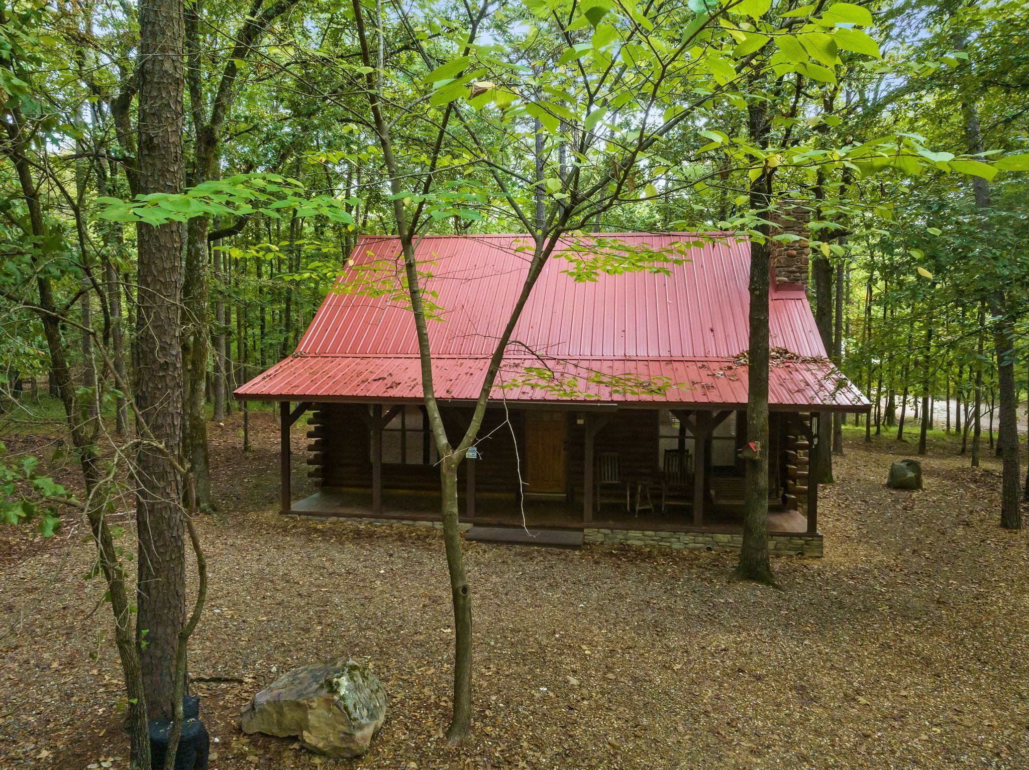 Una baita rustica con tetto rosso, immersa tra alberi e un vialetto sterrato.