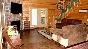 Ein gemütliches Blockhaus-Interieur mit Kamin aus Stein, Holzwänden, einem braunen Ledersofa und einer Treppe mit Girlandendekoration.