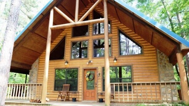 Eine Blockhütte mit Veranda, großen Fenstern und einem Steinfundament.