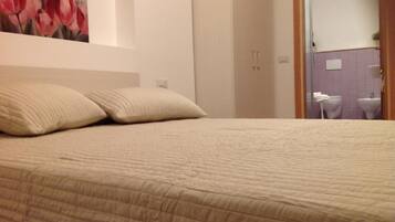 Una cama con colcha color crema, dos almohadas y un cuadro con tulipanes rojos en la pared.