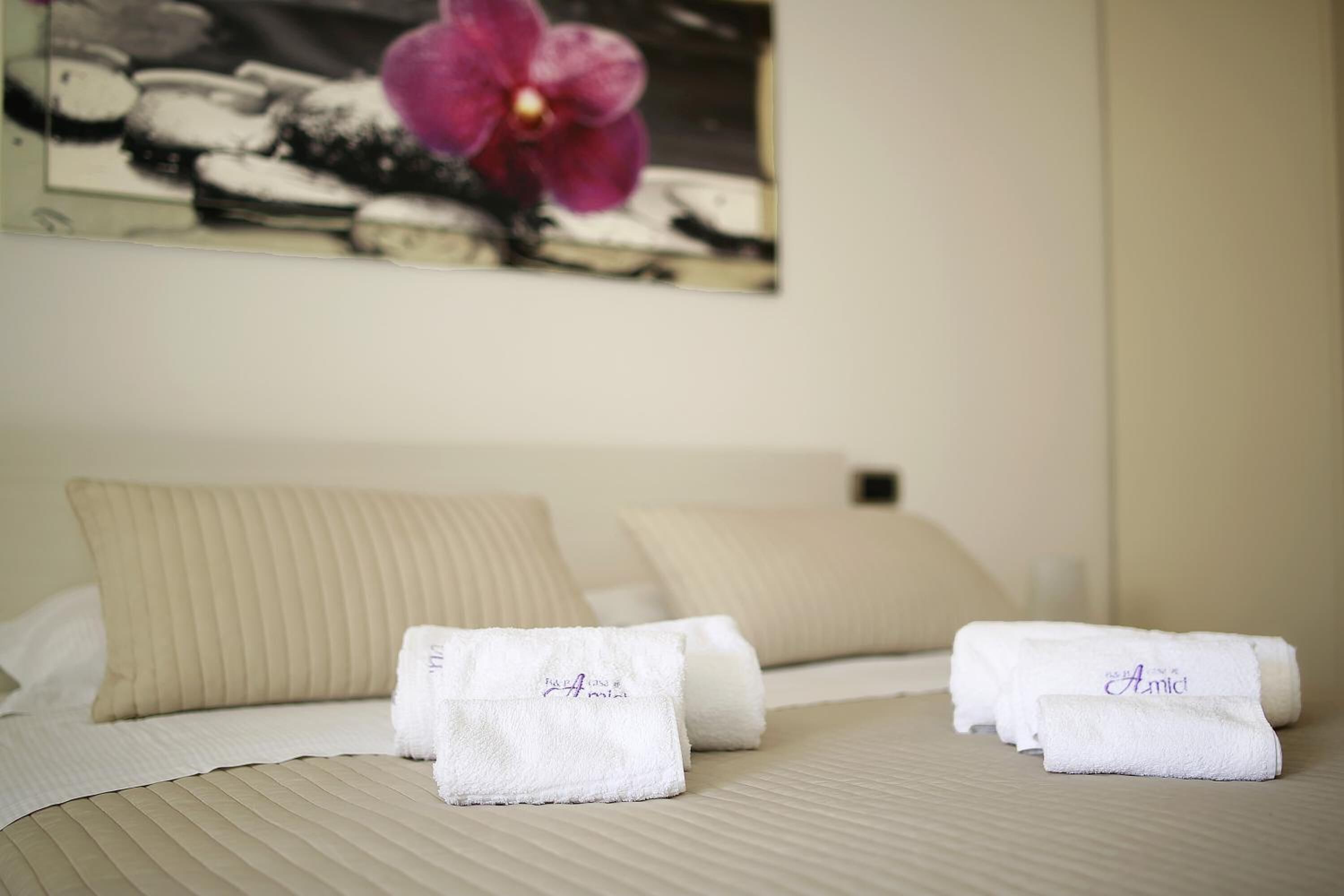 Een netjes opgemaakt bed met twee kussens, een witte handdoek en een ingelijste foto van een bloem aan de muur.