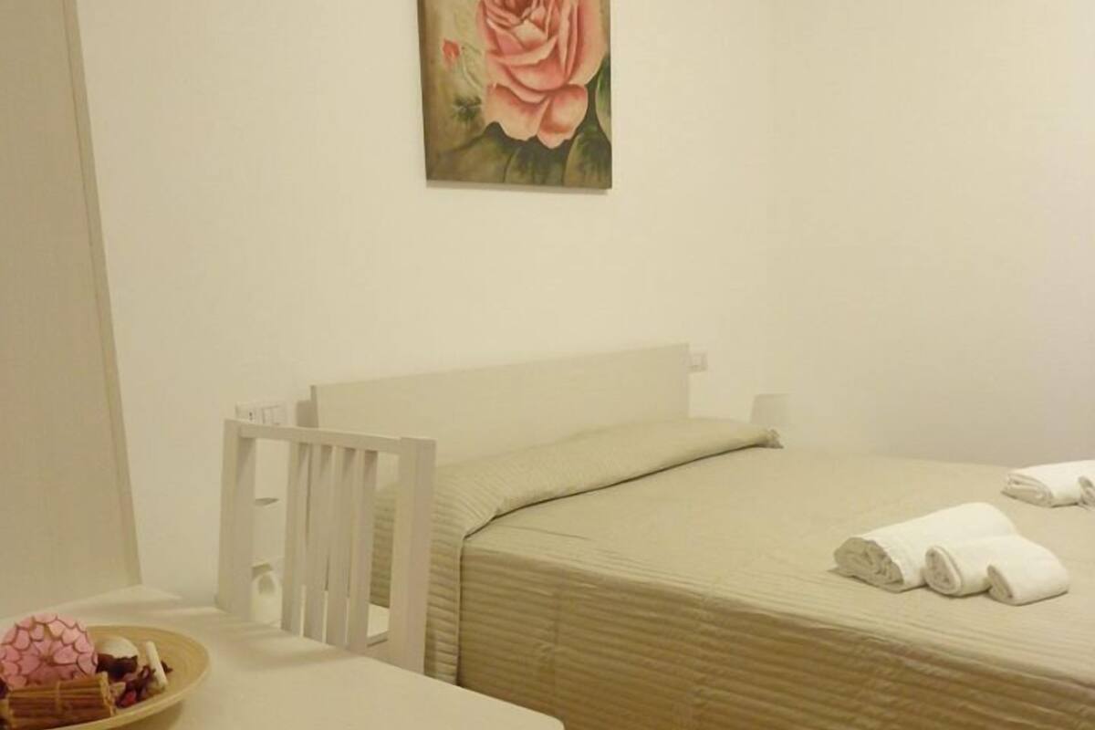 Una habitación pequeña y limpia con una cama, una mesa con un plato de comida y un cuadro de una rosa en la pared.