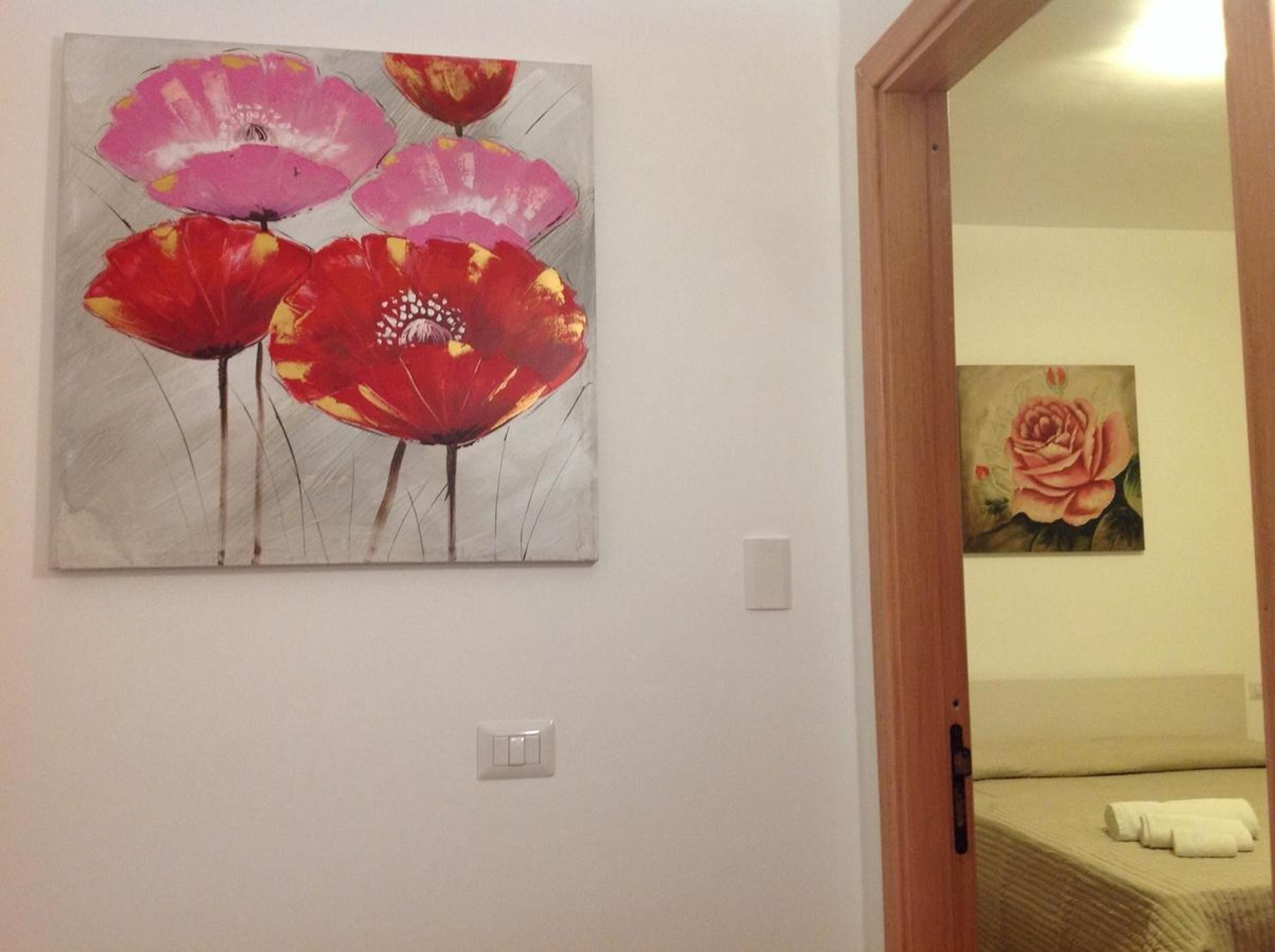 A hotel room with a bed, a painting of flowers on the wall, and a door leading to another room.