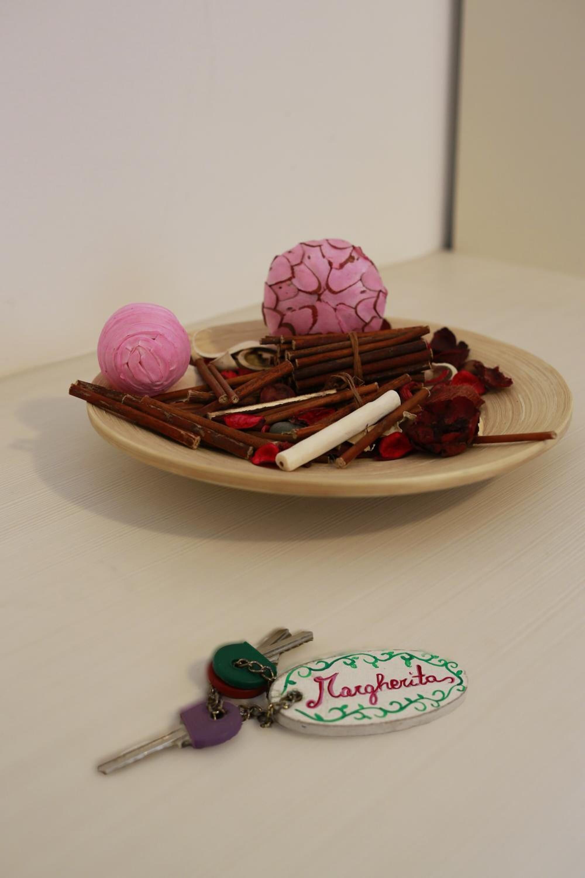 Un plato con diversos elementos, entre ellos una pelota rosa, flores secas y ramitas.
