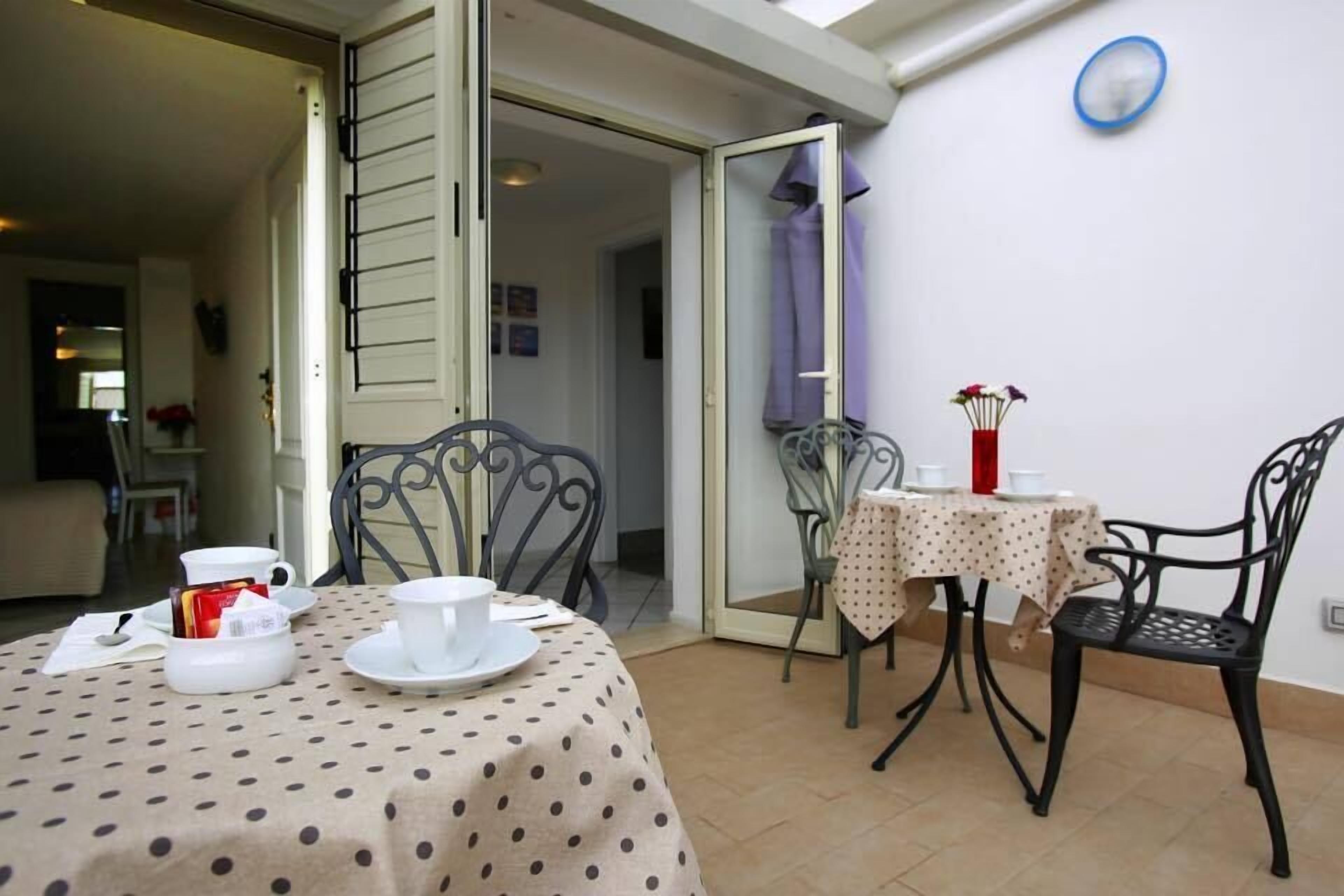 A dining area with a table set for two, a chair, and a small table with a vase of flowers.