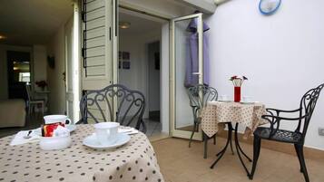 A dining area with a table set for two, a chair, and a small table with a vase of flowers.