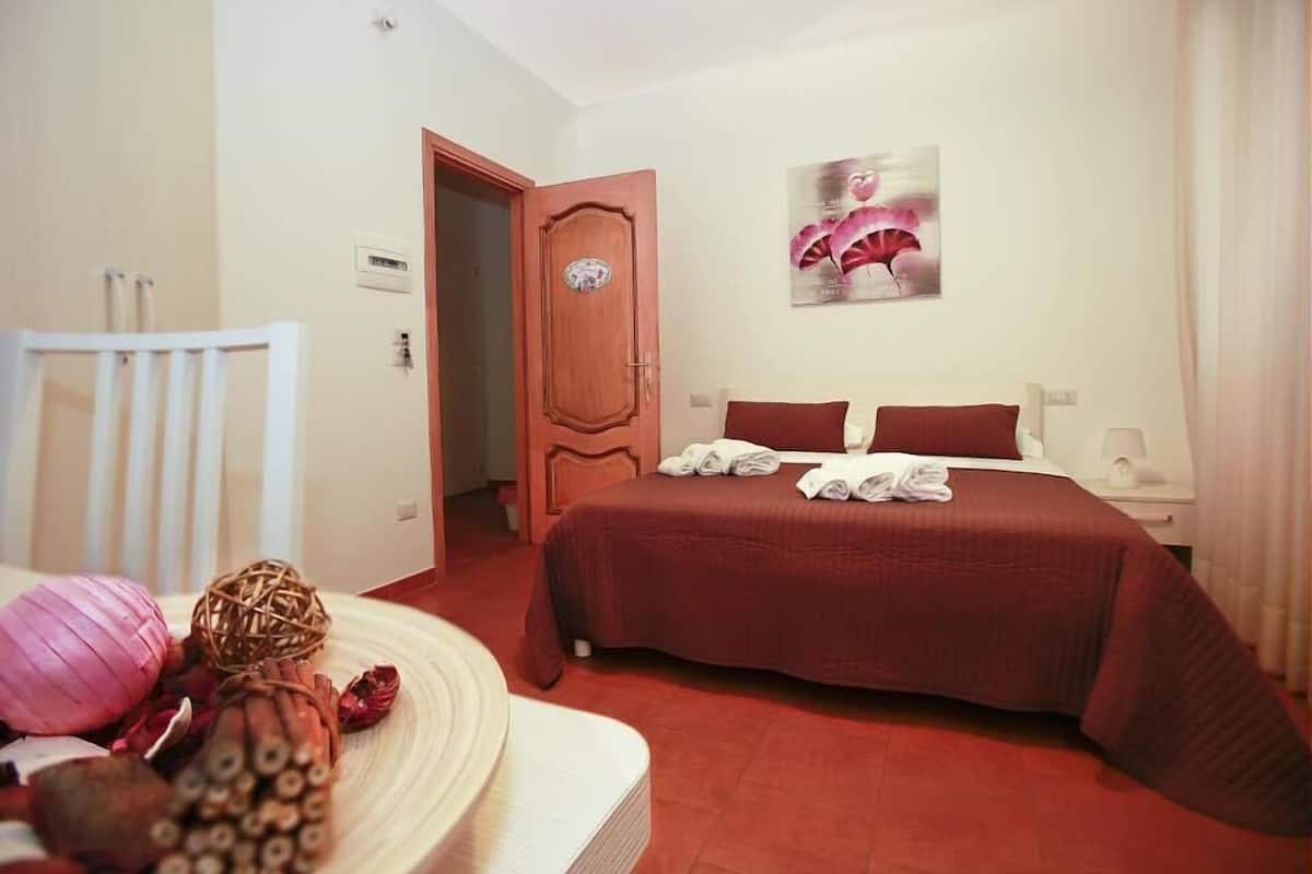 Una habitación de hotel con una cama, una puerta de madera, un cuadro en la pared y una silla blanca.