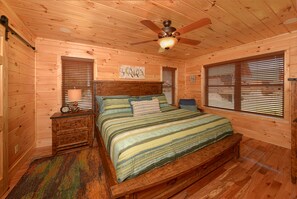 Ein Schlafzimmer einer Holzhütte mit Bett, Nachttisch und Deckenventilator.