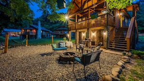 Un chalet rustique doté d’une cheminée en pierre, d’un espace salon extérieur et d’une terrasse en bois.