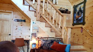 Un intérieur en bois avec un escalier, un canapé et un tableau représentant un ours dans un canoë.