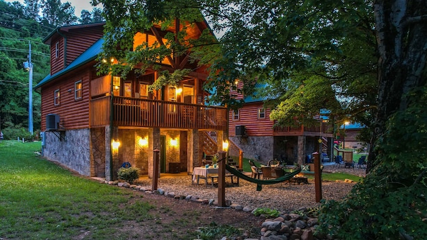 Une cabane en rondins avec des fondations en pierre, un balcon et un espace extérieur aménagé avec un hamac.