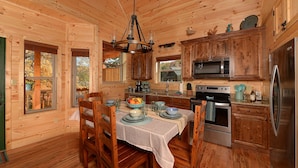 Une cuisine rustique aménagée dans une cabane en bois, avec une table à manger, des chaises, un lustre, des armoires en bois, un réfrigérateur et un four à micro-ondes.
