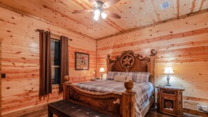 A wooden cabin bedroom with a bed, bench, ceiling fan, and two bedside tables.
