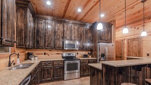 A kitchen with wooden cabinets, stainless steel appliances, granite countertops, and pendant lighting.