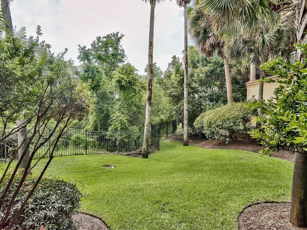 A well-maintained garden with a variety of trees and shrubs, a neatly trimmed lawn, and a metal fence.