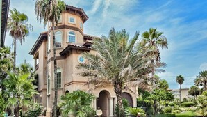 A large, multi-story building with a Mediterranean architectural style, surrounded by lush greenery and palm trees. - Short Walk to Beach • Pool • Pets Allowed • (Miramar Beach)