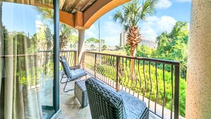 A balcony with wicker furniture, a view of greenery and buildings, and a clear sky. - Short Walk to Beach • Pool • Pets Allowed • (Miramar Beach)