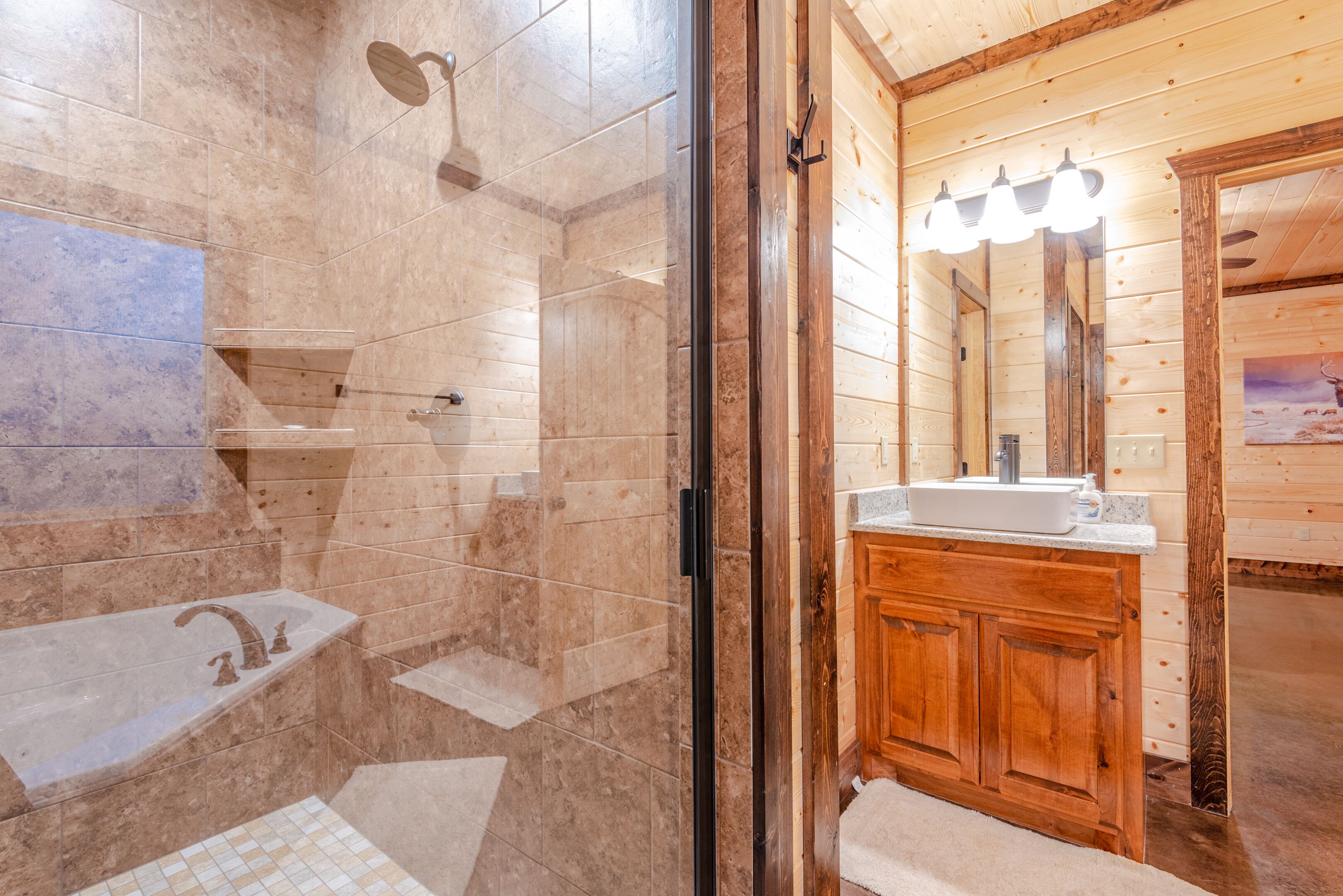 Une salle de bain dotée d’une douche à parois de verre, d’un mur recouvert de carreaux de marbre, d’un meuble-lavabo en bois et d’un miroir avec éclairage intégré.