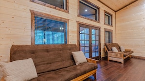 Una habitación acogedora con un sofá marrón, una silla de madera, ventanas amplias y paredes de madera.