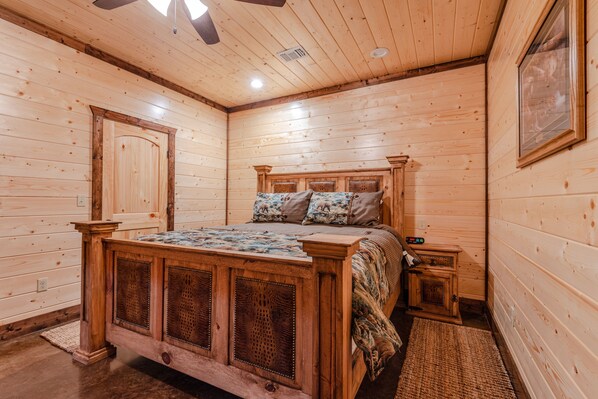 Un dormitorio de cabaña de madera con cama, mesitas de noche y una puerta.