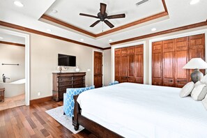 Une chambre à coucher avec un grand lit, une armoire en bois, un ventilateur de plafond et un téléviseur posé sur une commode.