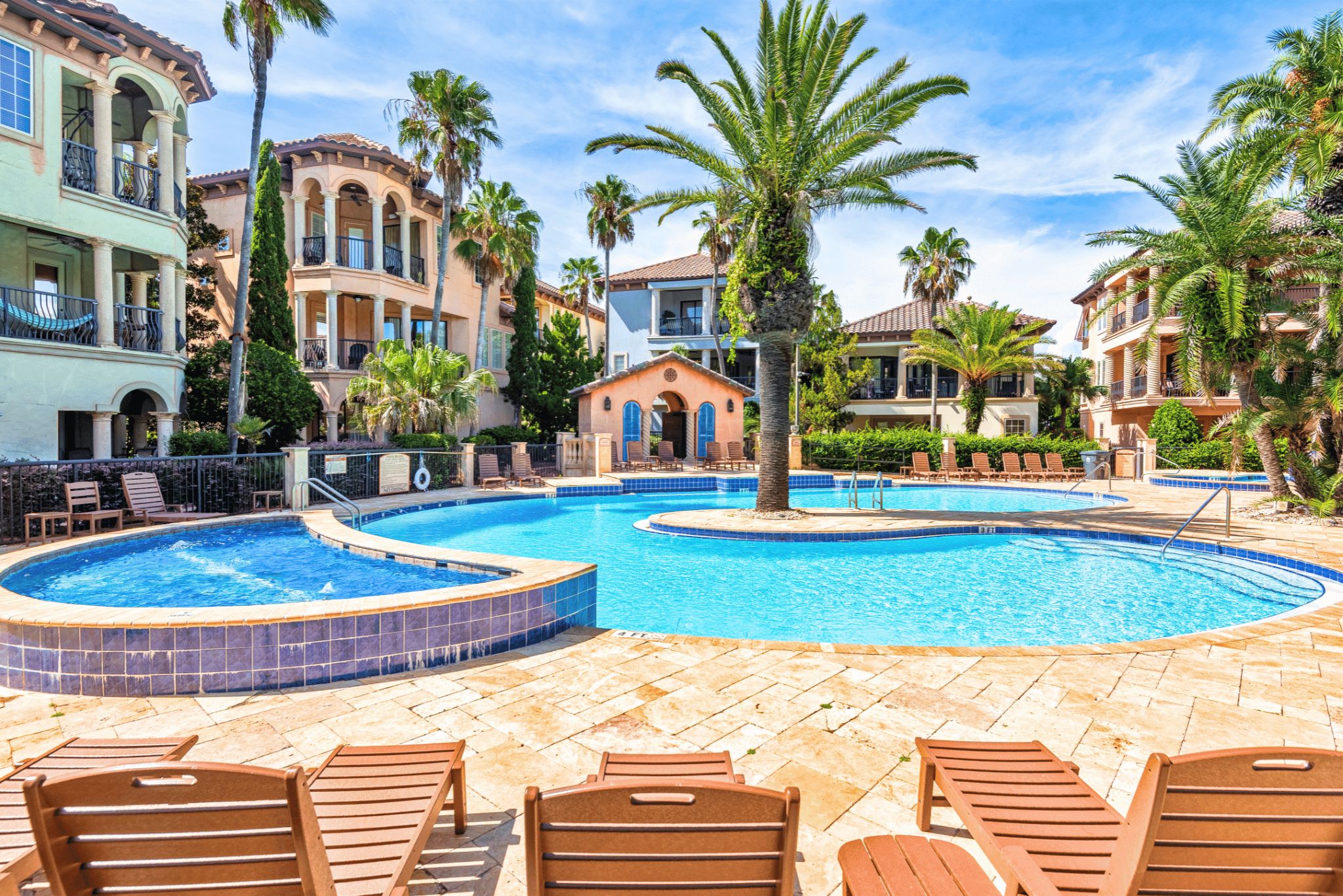 A resort pool area with multiple pools, lounge chairs, and palm trees.