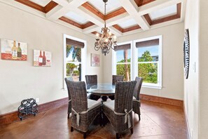 Un coin repas avec une table ronde, des chaises en osier, un lustre et de grandes fenêtres offrant une vue dégagée.