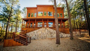 A two-story log cabin with a stone staircase leading to a wooden deck.