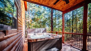 A hot tub on a wooden deck with a view of a forest.