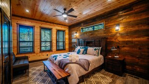 A wooden cabin bedroom with a bed, bench, and two windows.