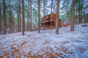 Eine Holzhütte, umgeben von hoch aufragenden Kiefern in einem verschneiten Wald.