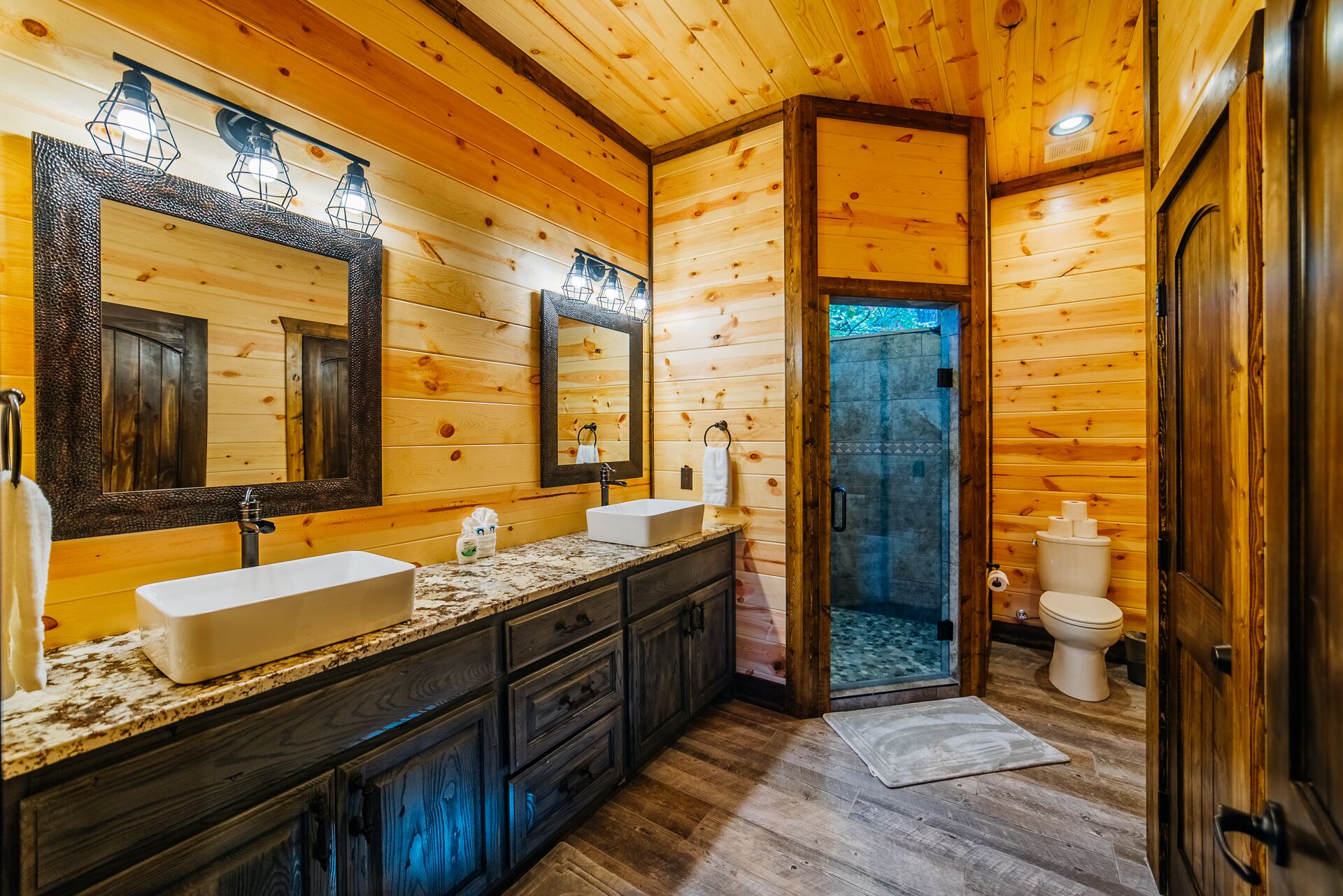 A wooden cabin bathroom with two sinks, a large mirror, and a shower area.