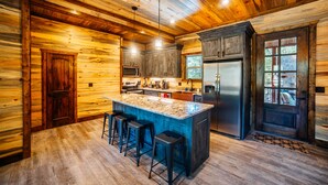 A log cabin kitchen with a central island, bar stools, a refrigerator, and wooden walls.