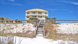 A beachfront building with a staircase leading to the entrance, surrounded by sand and sparse vegetation.