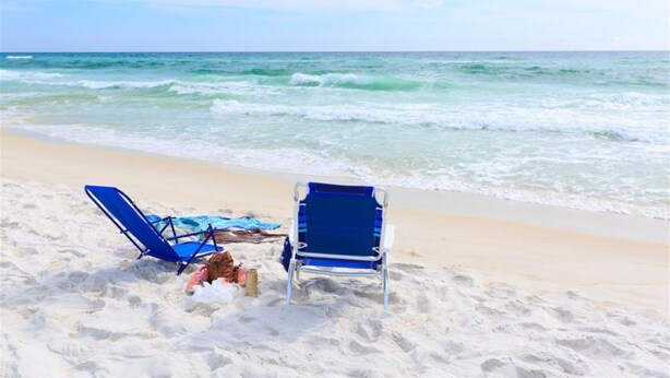 Two blue beach chairs on a sandy beach with a clear view of the ocean.
