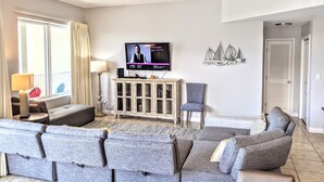 A modern living room with a flat-screen TV, a ceiling fan, and a decorative wall piece.