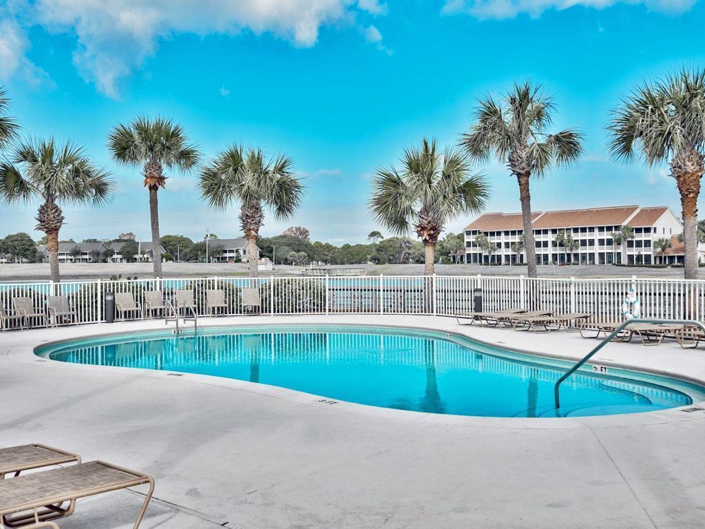 A swimming pool with lounge chairs and palm trees, surrounded by a white fence.