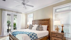 A bedroom with a wooden bed, two bedside tables, a ceiling fan, and a view of the outdoors through a sliding door.