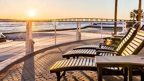 En uteplats vid stranden med solstolar och utsikt över havet vid solnedgången.