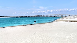 En strand med en brygga som sträcker sig ut i vattnet, en sandstrand och en klar himmel.